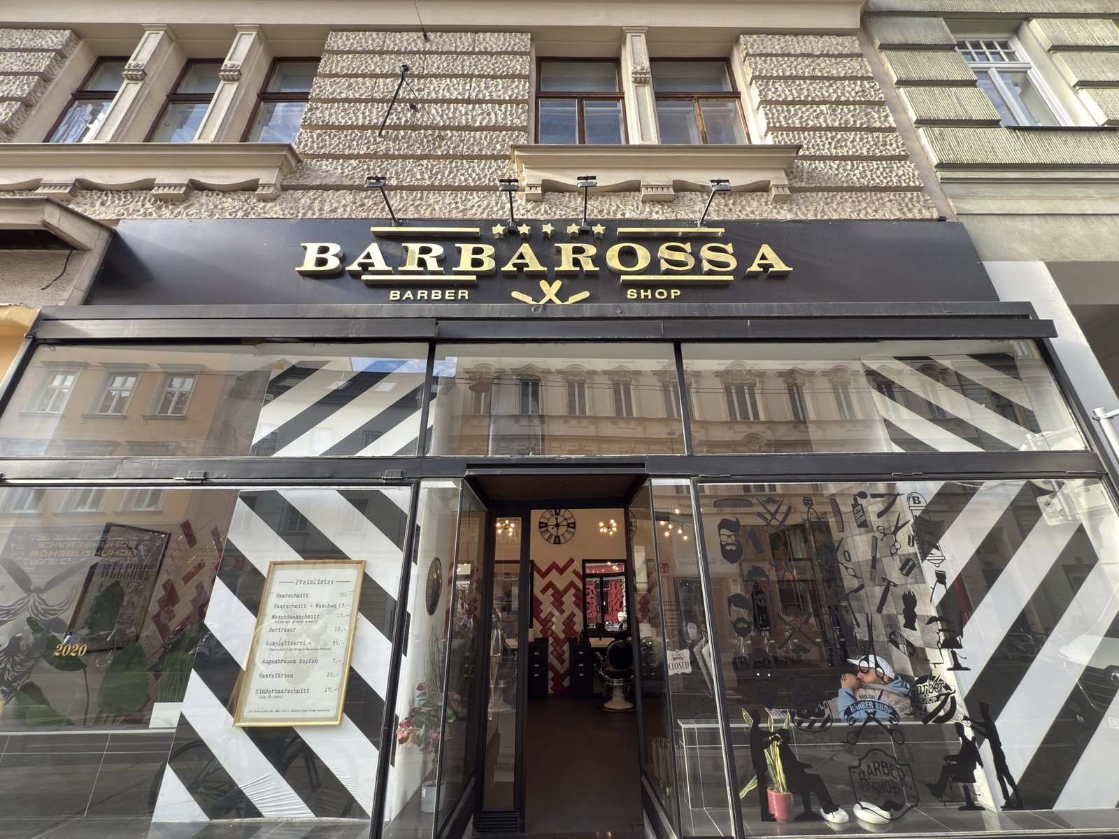 Außenansicht des Salons in der Margaretenstraße mit schwarz-goldener Barbarossa-Tafel und schwarz-weiß gestreiften Schaufenstern